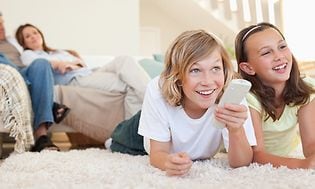 mann kvinne og to barn smiler samlet foran tv med fjernkontroll i hånd