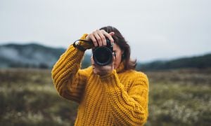 kvinne i gul genser i fjellandskap fotograferer med kamera