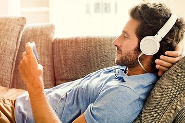 Mann ligger på sofa med smarttelefon i hånden og headset på hodet