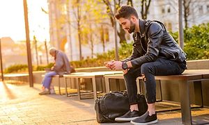 To menn sitter ute på parkbenk og ser på hver sin smarttelefon