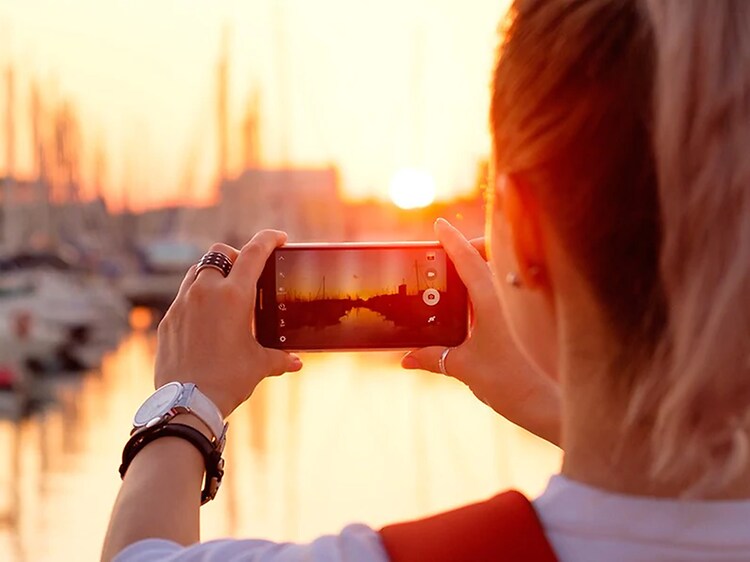 kvinne fotograferer solnedgang over havn med smarttelefon