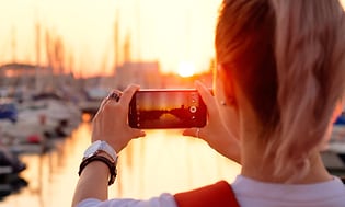 kvinne fotograferer solnedgang over havn med smarttelefon