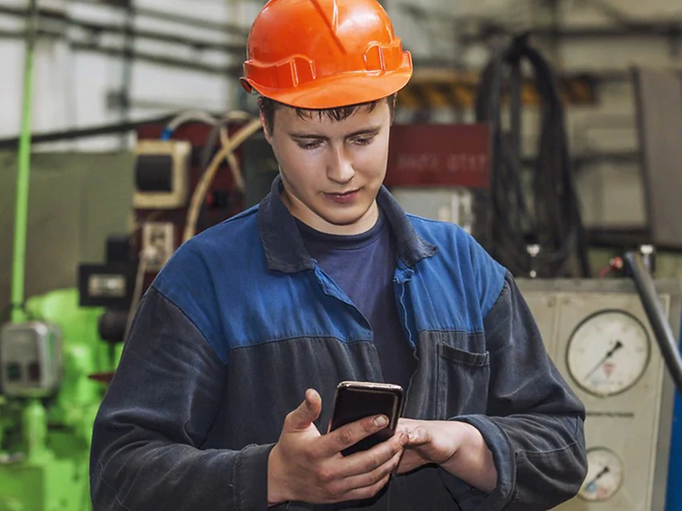 mann ser på robust smarttelefon i arbeidsuniform med hjelm på