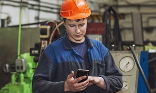 mann ser på robust smarttelefon i arbeidsuniform med hjelm på
