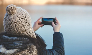 kvinne med lue og vinterjakke fotograferer med smarttelefon