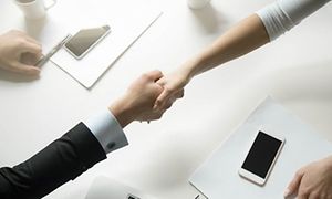 to personer tar hverandre i hendene over et bord med smarttelefoner og papirer