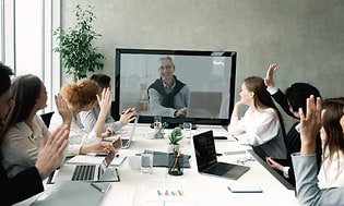 møterom med flere mennesker og en mann med på videomøte via skjerm