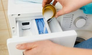 nærbilde av person som heller vaskemiddel inn i vaskemaskin