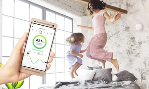 smarttelefon med en luftmåler i frorgrunn og barn som hopper i en seng i bakgrunnen