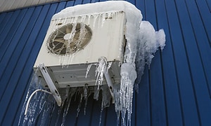 varmepumpe montert utendørs på vegg med mye snø og is på seg