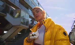 Jente med gul jakke og Polaroid Go-kamera 